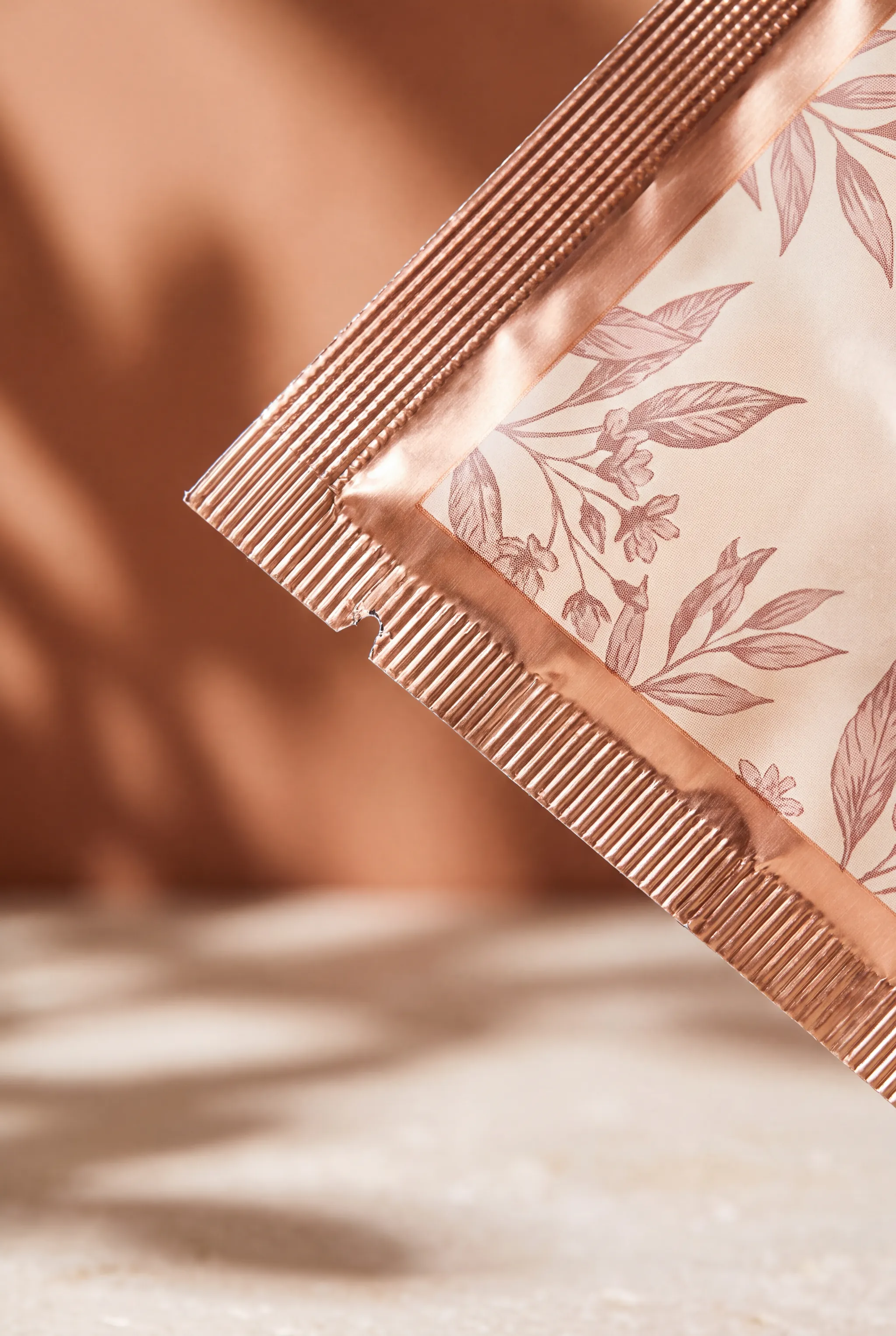 Macro view of a sachet corner where two finely crimped seals meet, the parallel ridges of the crimping tool visible and a foil sheen under the printed pattern.